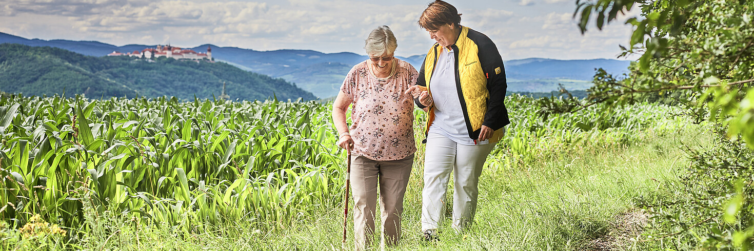 Hilfswerkerin spaziert mit einer älteren Dame auf einem Feldweg