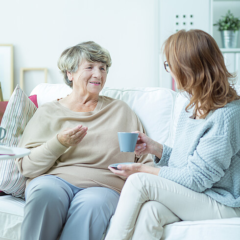 Ältere und jüngere Frau trinken Kaffee auf dem Sofa.