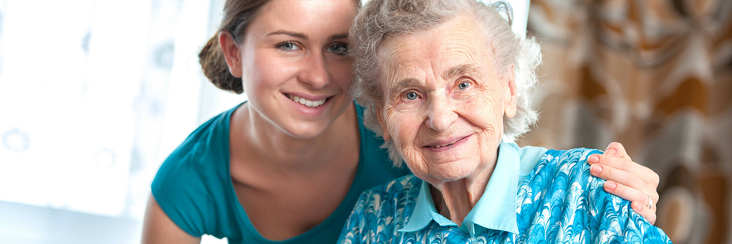 Ältere Dame und Pflegerin lächeln in die Kamera