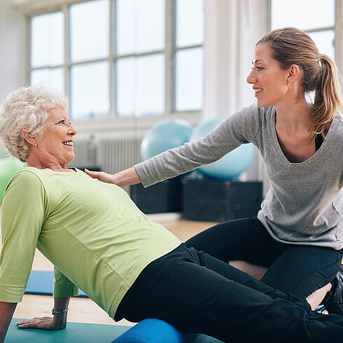 Fitnesstrainerin erklärt einer Frau eine Übung auf der Matte