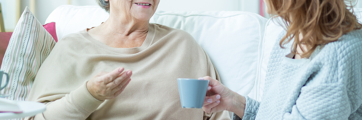 Ältere und jüngere Frau trinken Kaffee auf dem Sofa.