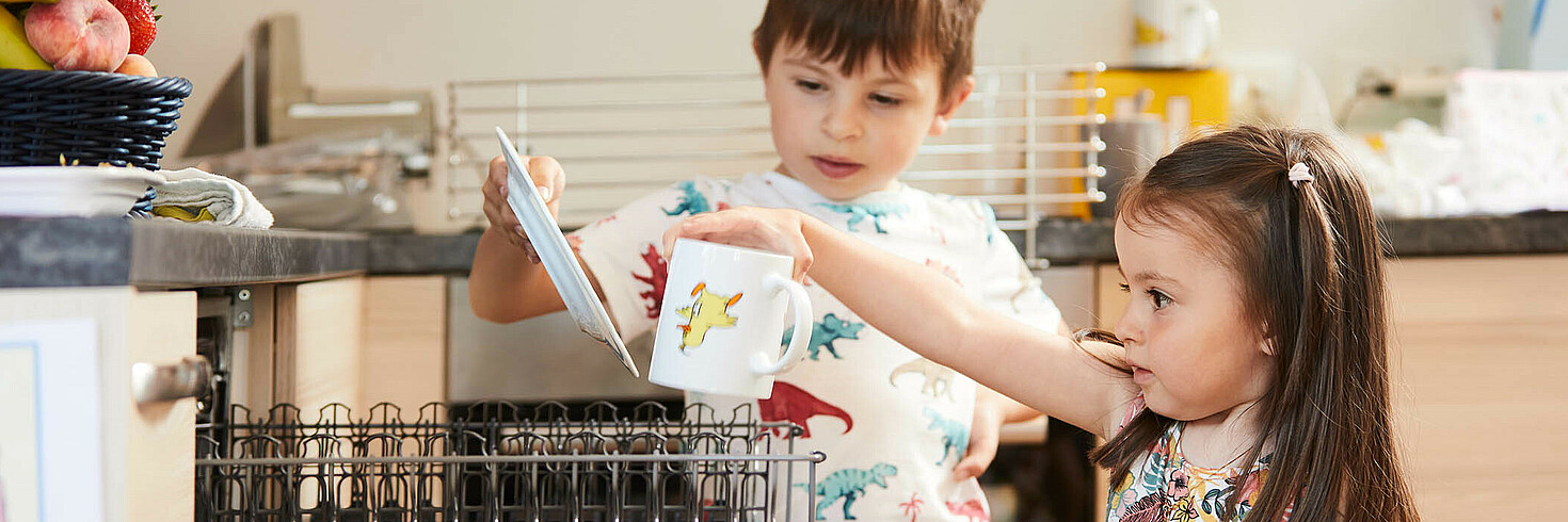 Zwei Kinder im Vorschulalter räumen konzentriert ihre Tassen in die Geschirrwaschmaschine