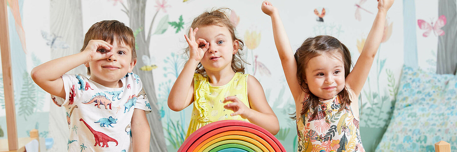 Drei Kinder im Vorschulalter formen mit den Händen ein Fernrohr und gucken durch