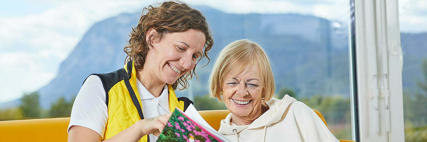 Eine Hilfswerk Betreuerin und eine Seniorin lesen ein Buch.