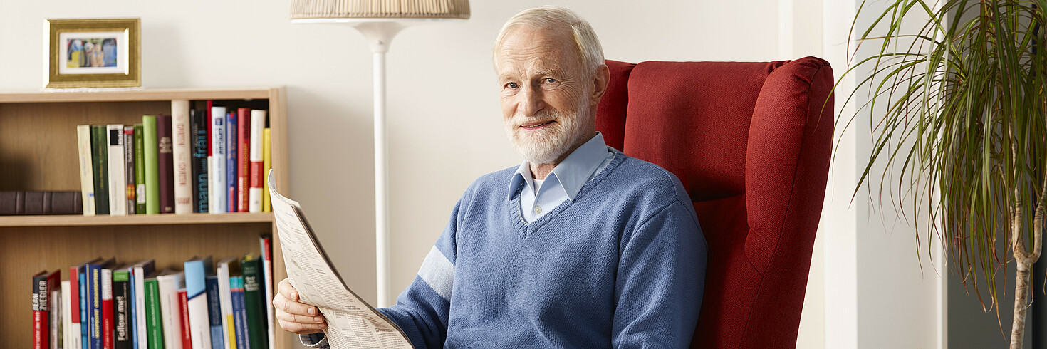 Älterer Herr sitzt Zeitung lesend in einem bequemen Sessel.