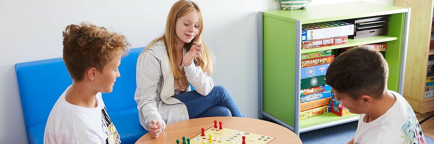 Zwei Burschen und ein Mädchen im Sekundarschulalter beim Brettspiel in der Schülernachmittagsbetreuung