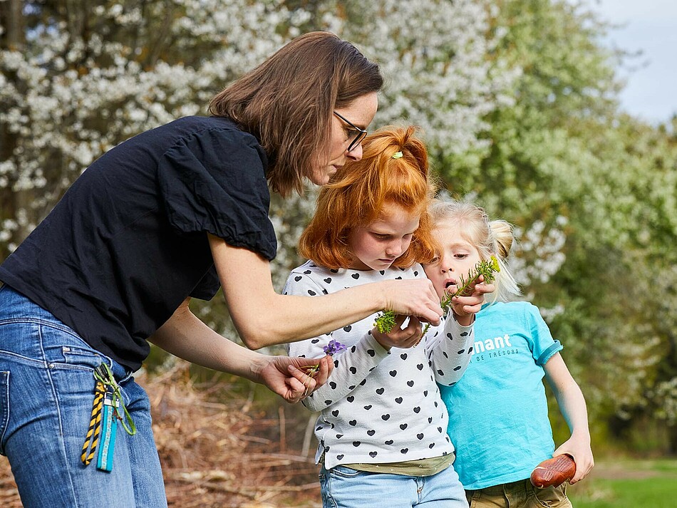 Mutter und zwei Kinder im Freien betrachten eine Blüte 