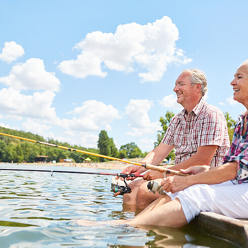 Älteres Paar sitzt am Ufer und angelt