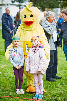 Maskottchen FIDI und 2 Mädchen lächeln.