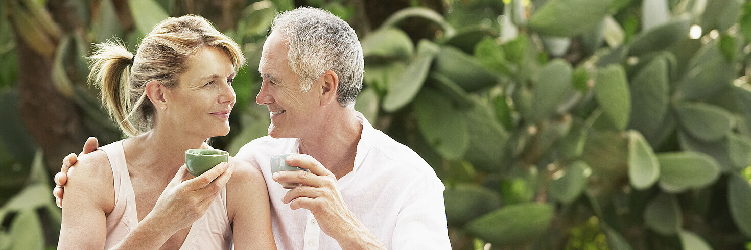 Paar mittleren Alters beim Tee Trinken, im Hintergrund Kakteen, die beiden schauen sich an und lächeln
