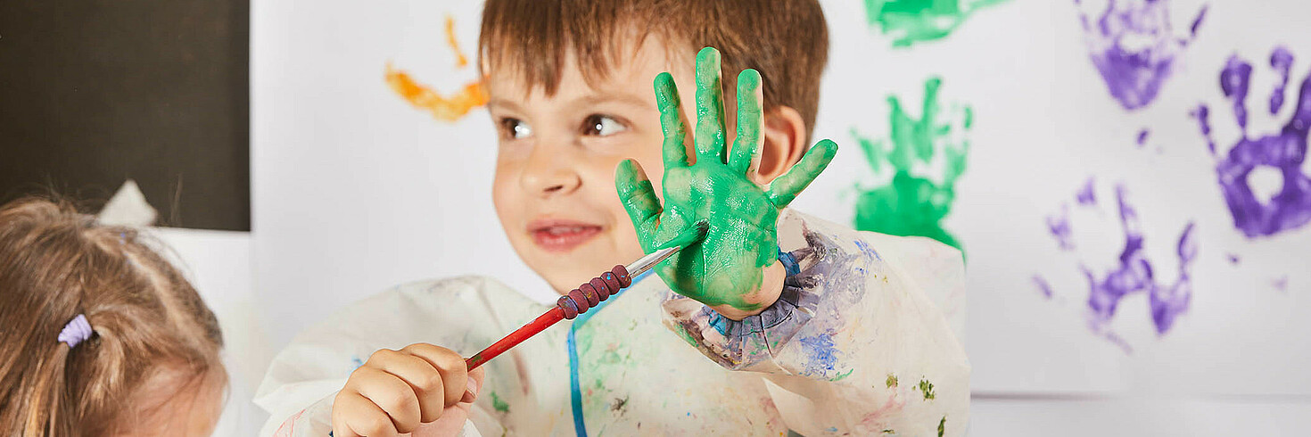 Bub im Vorschulalter zeigt stolz seine grün bemalte Handfläche 