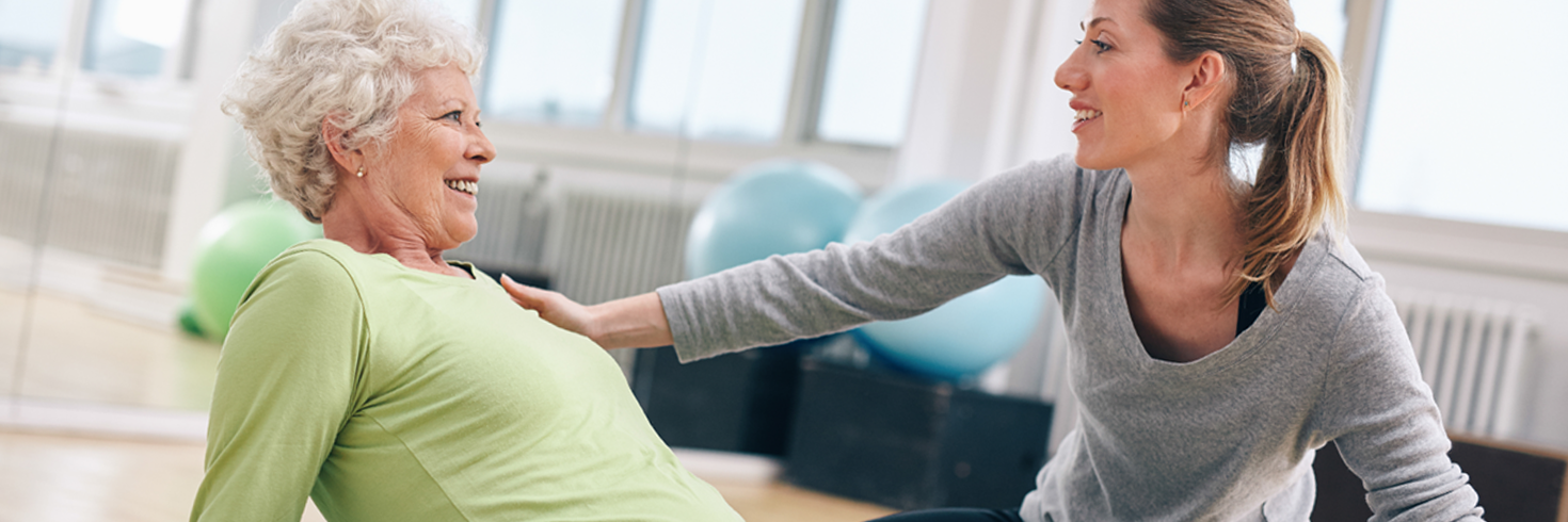 Fitnesstrainerin erklärt einer Frau eine Übung auf der Matte