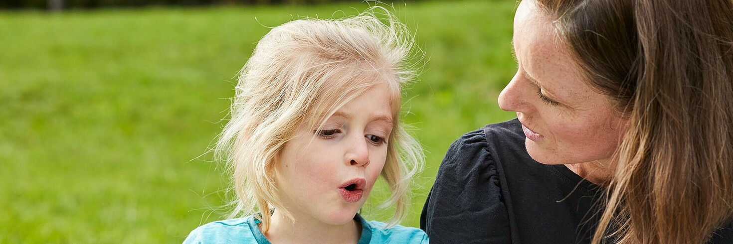 Mutter sitzt mit Kind auf einer Wiese, das Kind erzählt etwas