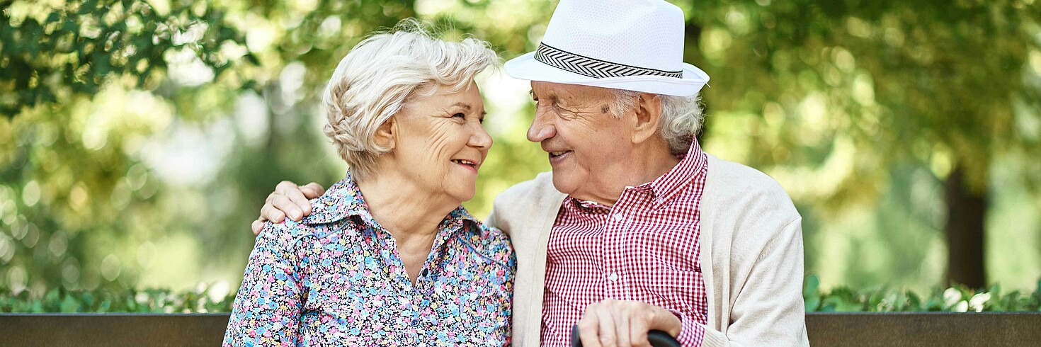 Älteres Paar sitzt lächelnd auf einer Parkbank
