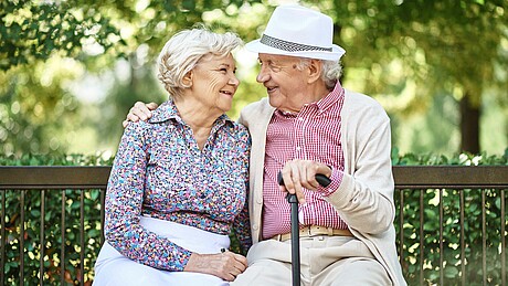 Älteres Paar sitzt lächelnd auf einer Parkbank