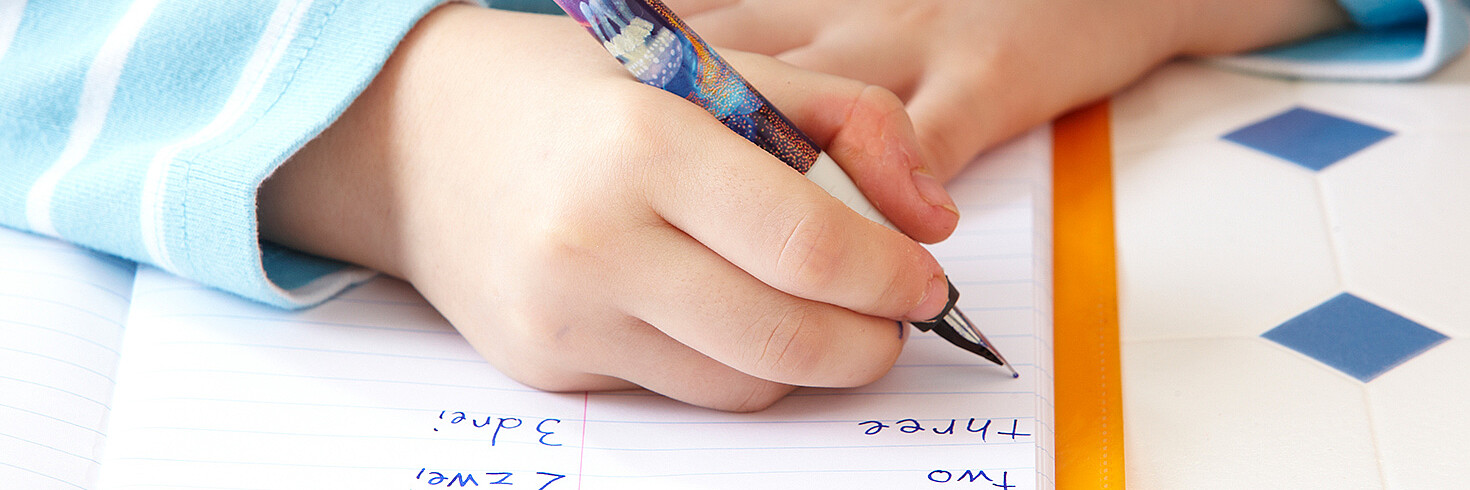 Ein Kind schreibt mit der Füllfeder englische Zahlen in ein Heft