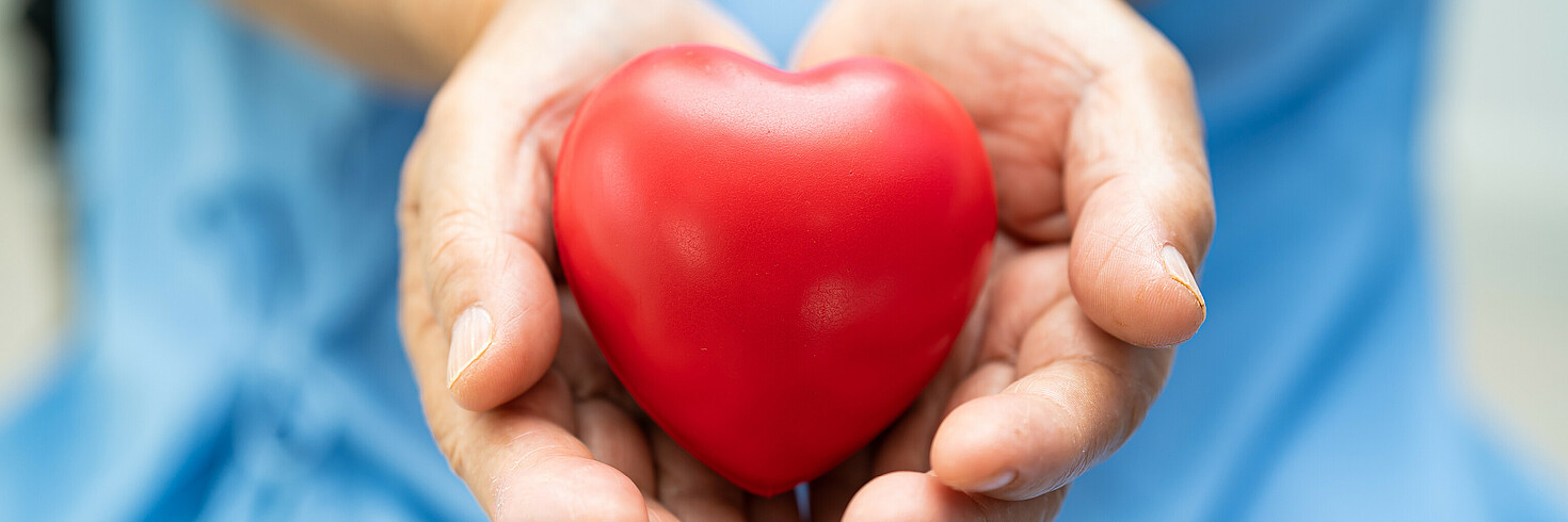 Hände halten rote Herzform.