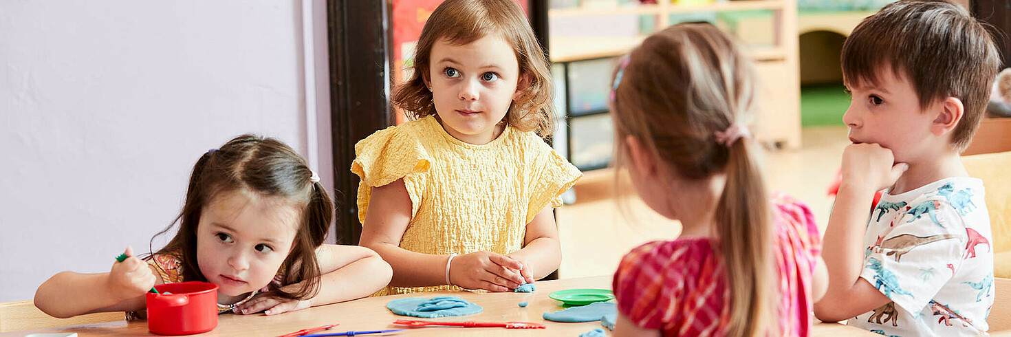 Kindergruppe am Tisch sitzend spielt mit bunter Knetmasse
