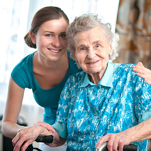 Ältere Dame und Pflegerin lächeln in die Kamera