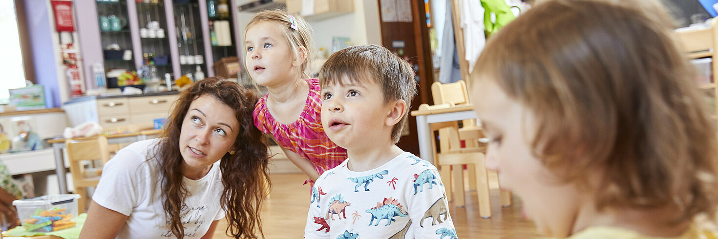 Kinder in Gruppe betrachten etwas mit Betreuerin.