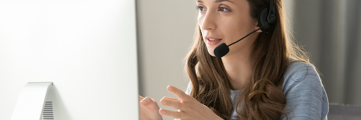 Lächelnde Frau mit Headset vor Bildschirm, mit Händen gestikulierend