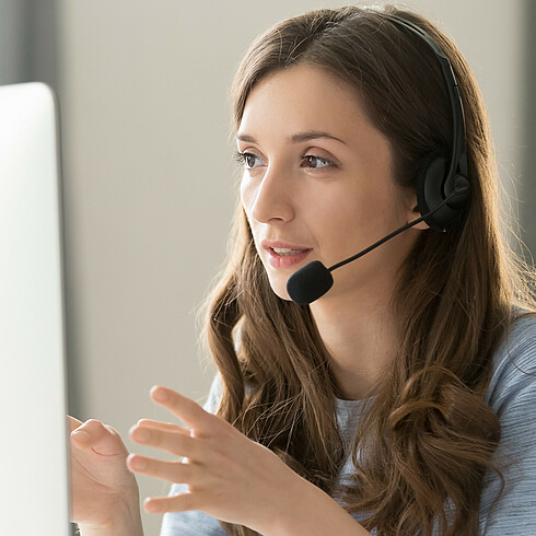 Lächelnde Frau mit Headset vor Bildschirm, mit Händen gestikulierend