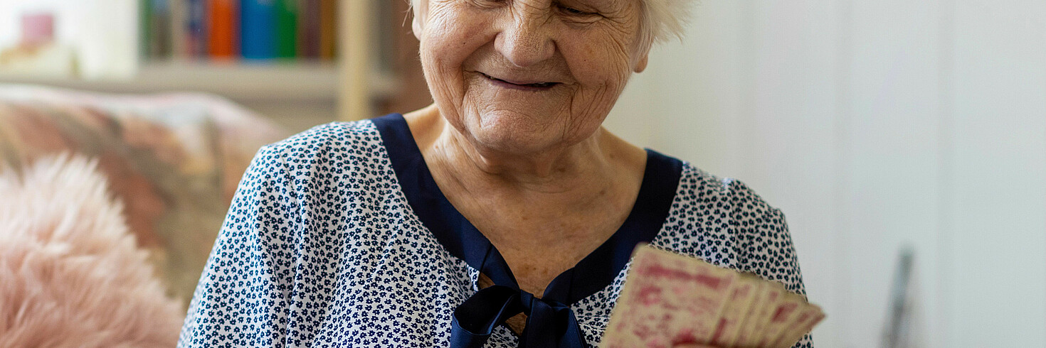 Hochbetagte Dame sitzt am Sofa und spielt mit ihrer 24-Stunden-Betreuerin Karten
