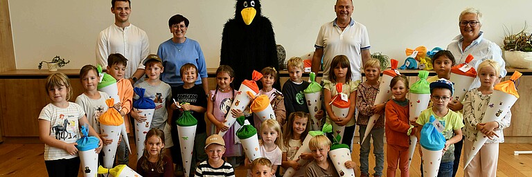 Schulanfänger mit Schultüten und Maskottchen "Rabe Socke" in einer Schule