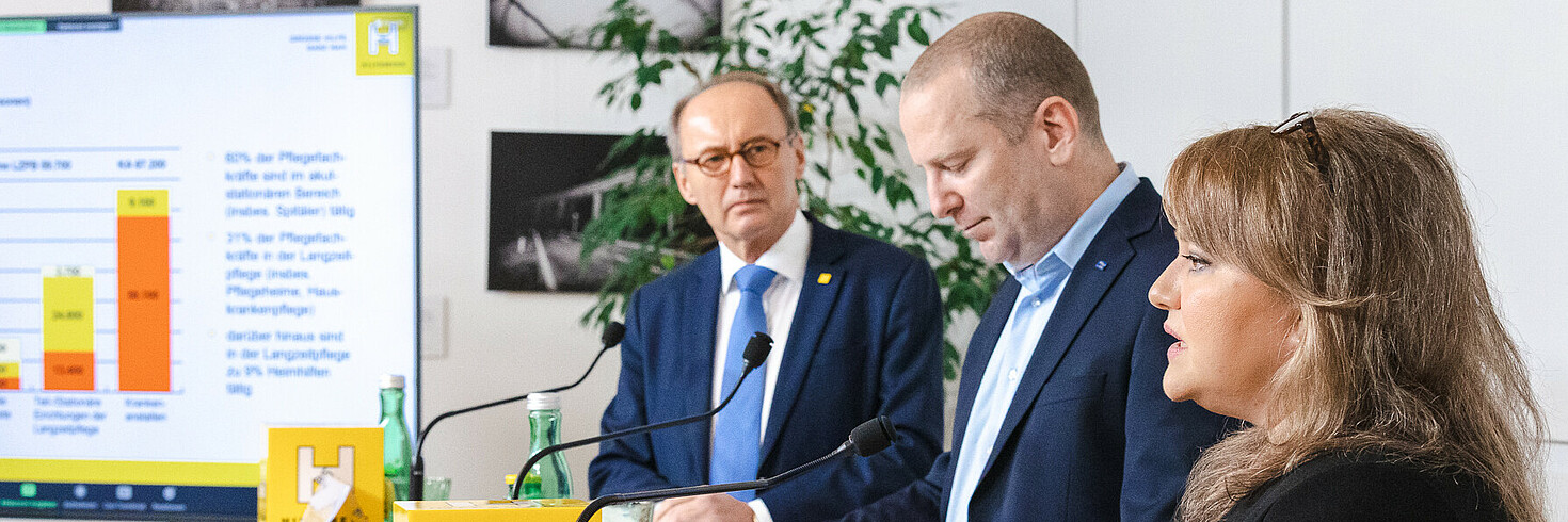 Eine Redner und zwei Redner bei einer Pressekonferenz an Stehpulten stehend