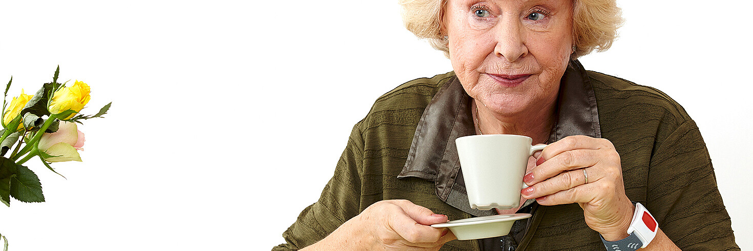Ältere Dame trinkt Kaffee und hat einen Notruftelefonsender am Handgelenk
