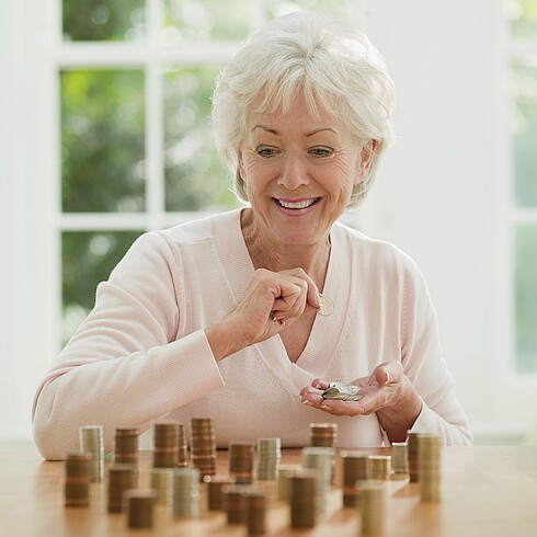 Ältere Dame sitzt an einem Tisch und zählt Münzen.