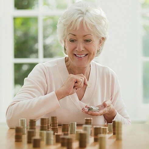 Ältere Dame sitzt an einem Tisch und zählt Münzen.