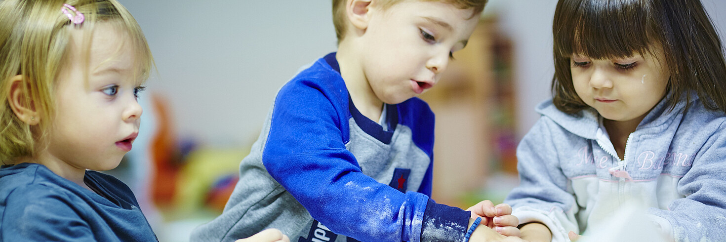 Kleine Kinder sitzen beim Backen um einen Tisch herum.