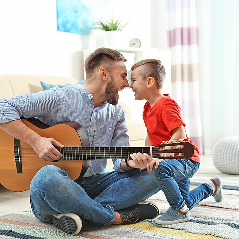 Vater spielt auf Gitarre, Vater und Sohn lachen