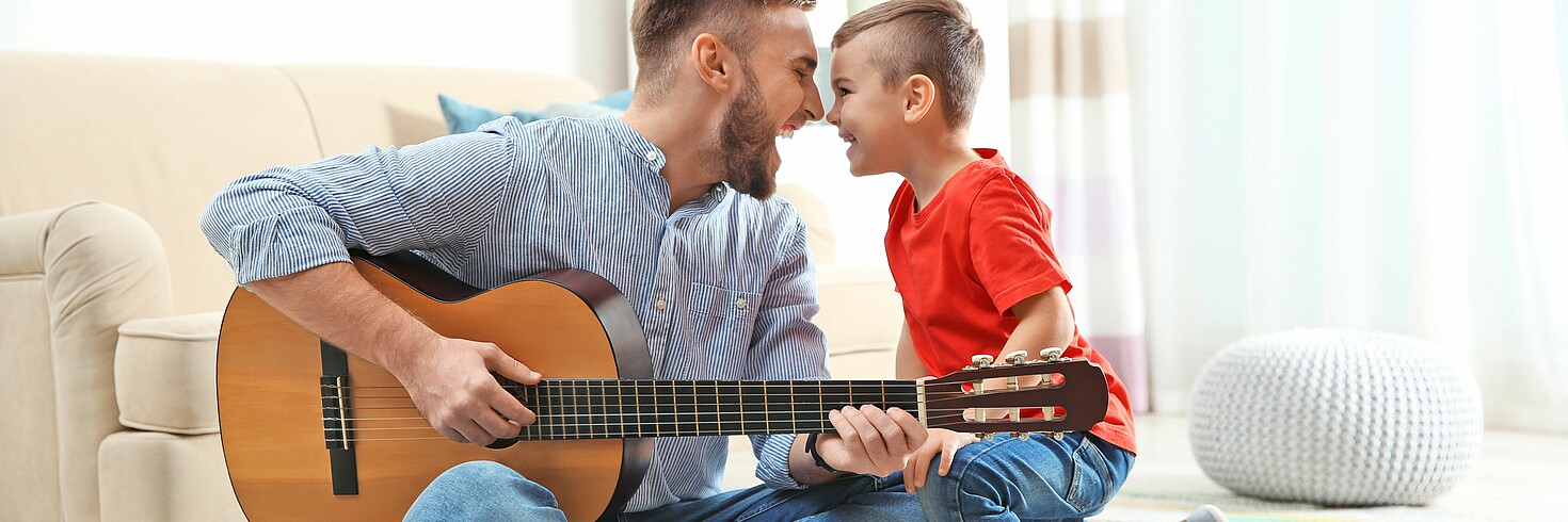 Vater spielt auf Gitarre, Vater und Sohn lachen