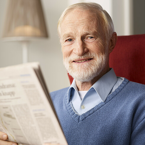 Älterer Herr sitzt Zeitung lesend in einem bequemen Sessel.