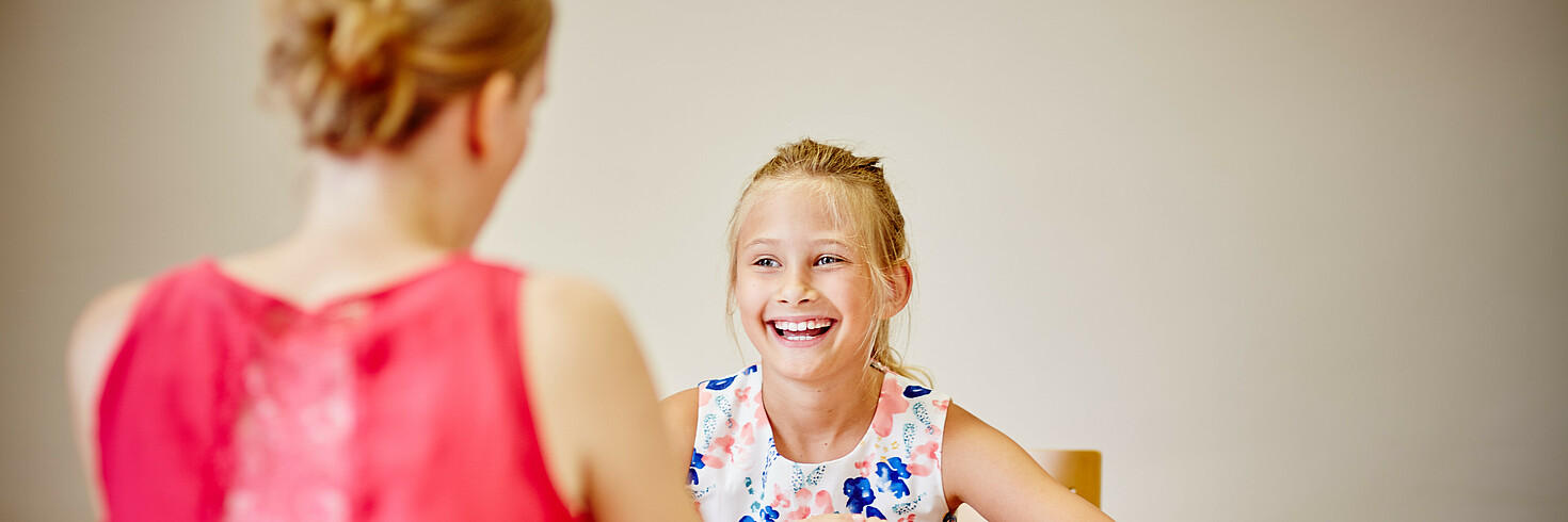 Ein junges Mädchen und eine Kinderbetreuerin sitzen an einem Tisch.