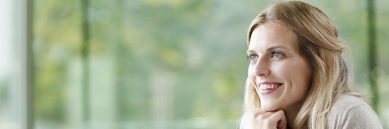 Junge Frau am Computer sitzend schaut lächelnd aus dem Fenster 