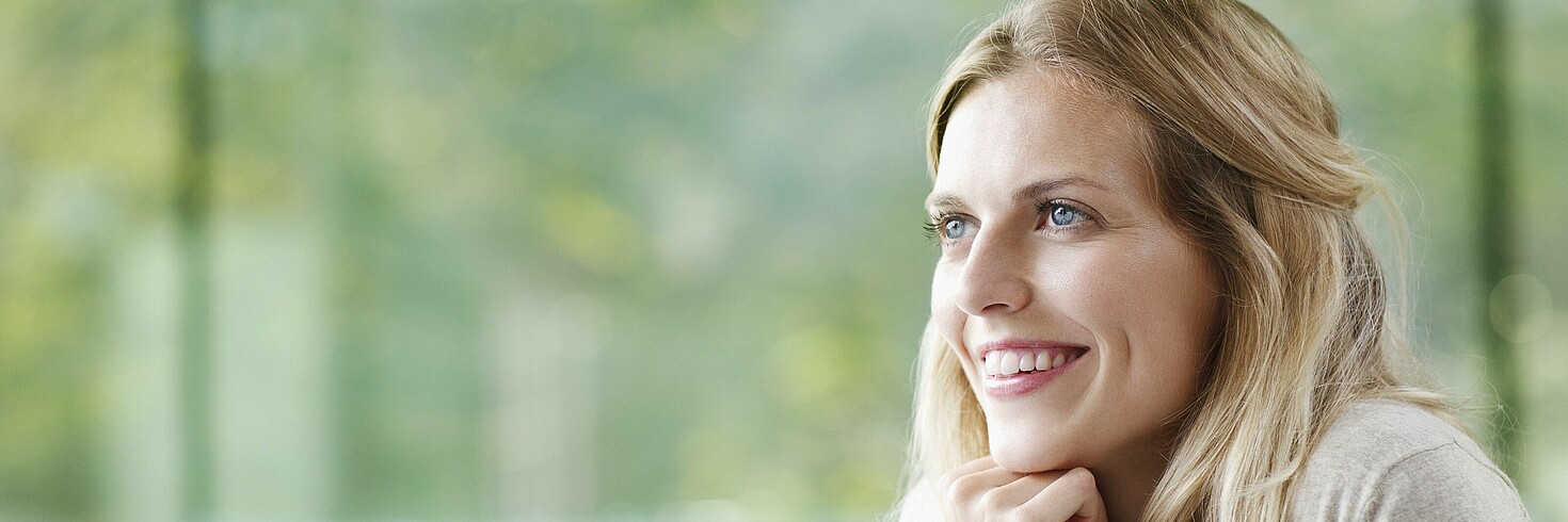 Junge Frau am Computer sitzend schaut lächelnd aus dem Fenster 