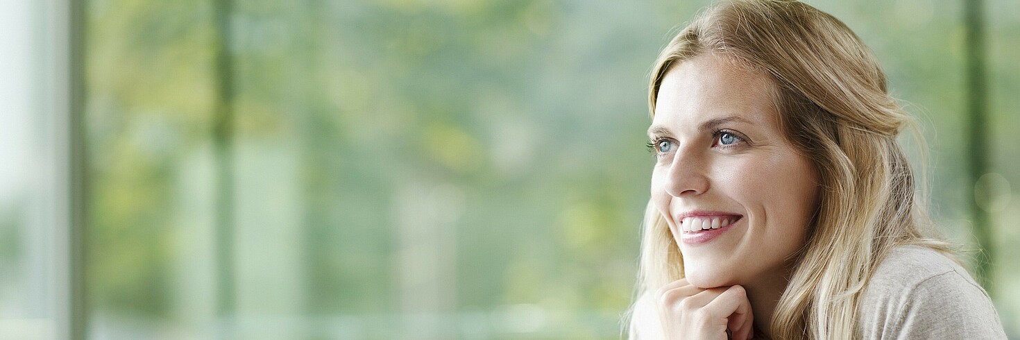 Junge Frau am Computer sitzend schaut lächelnd aus dem Fenster 