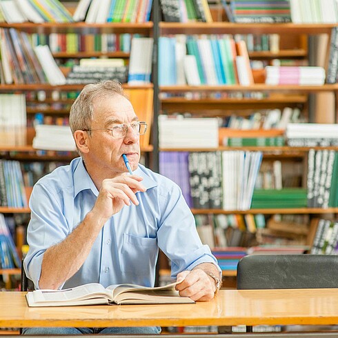 Mann mittleren Alters nachdenklich vor einem Bücherregal.