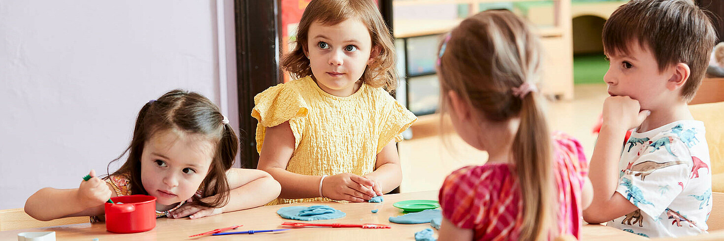 Kindergruppe am Tisch sitzend spielt mit bunter Knetmasse