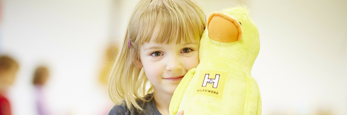 Ein kleines Mädchen mit einer FIDI-Plüschfigur in der Hand.