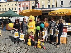Eine große Gruppe Menschen mit Plüschente in Lebensgröße posieren für die Kamera