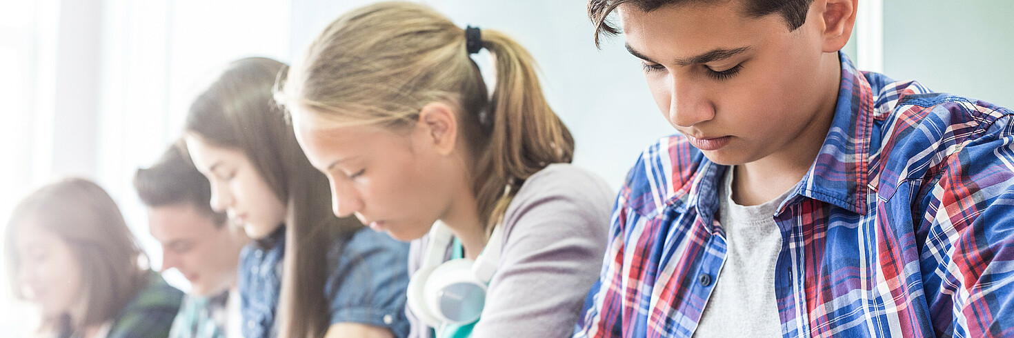 Vier Jugendliche sitzen nebeneinander über ihre Schulhefte gebeugt am Lernen