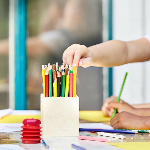 Nahaufnahme einer Kinderhand, die nach Bundstiften greift