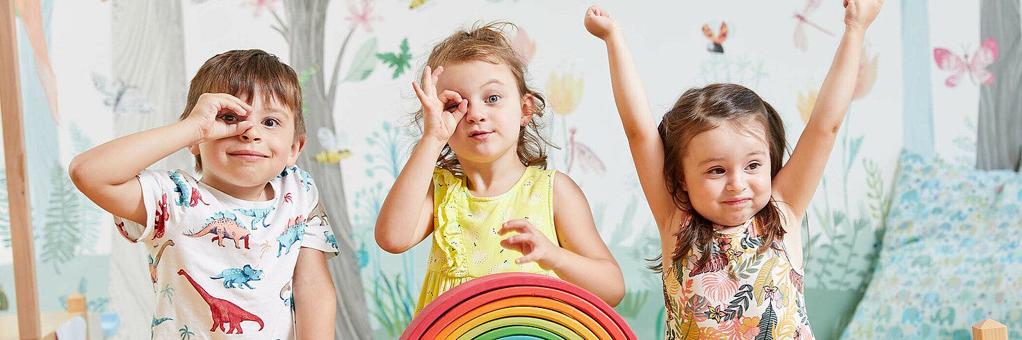 Drei Kinder im Vorschulalter formen mit den Händen ein Fernrohr und gucken durch