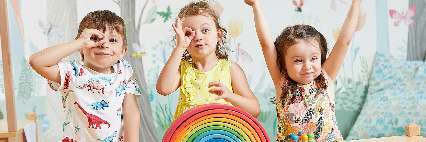 Drei Kinder im Vorschulalter formen mit den Händen ein Fernrohr und gucken durch