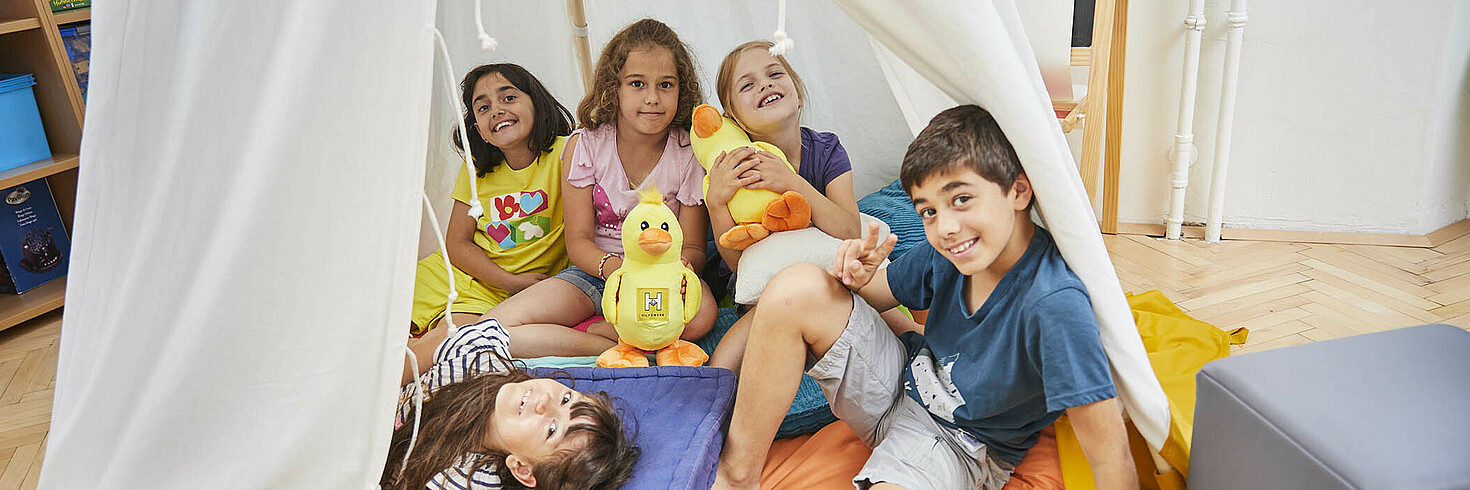 Kindergruppe sitzt und liegt auf Kissen in Kindertipi, alle lachen in die Kamera