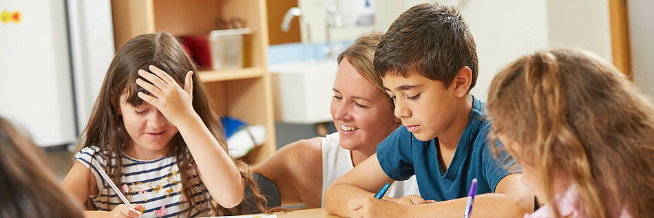 Eine Gruppe Schülerinnen und Schüler im Volksschulalter wird von Freizeitpädagogin beim Lernen unterstützt